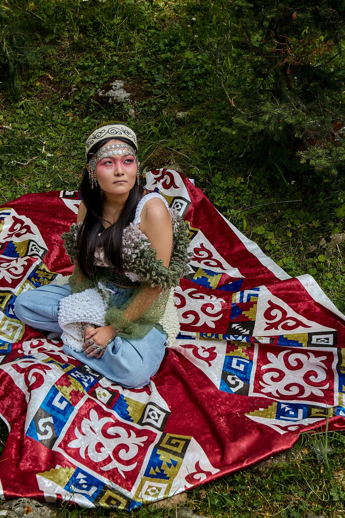Model seated on a Kyrgyz shyrdak carpet in the grass